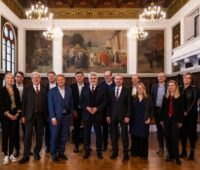 Zwölf weiße Männer und vier weiße Frauen in dunklen Anzügen in einem Festsaal - Energieminister-Konferenz in Merseburg.
