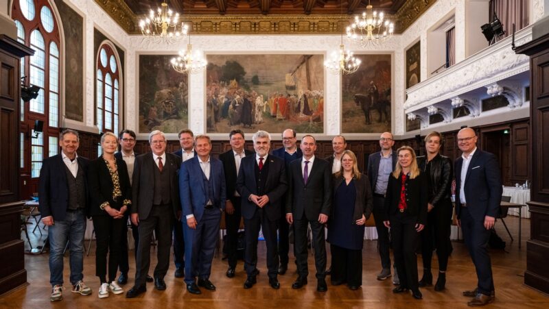 Zwölf weiße Männer und vier weiße Frauen in dunklen Anzügen in einem Festsaal - Energieminister-Konferenz in Merseburg.