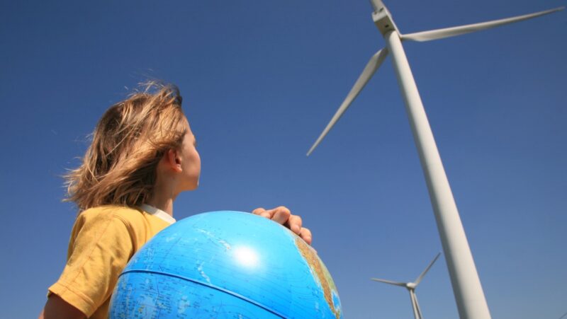 Ein Kind mit einer Weltkugel neben Windkraftanlagen, als Symbol für Energieerzeugung, erneuerbare Energien, Kohleausstieg