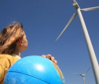 Ein Kind mit einer Weltkugel neben Windkraftanlagen, als Symbol für Bürgerbeteiligung, Bürgerenergie, Windenergie, Energiewende.