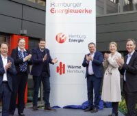 Vier Männer und zwei Frauen stehen neben einem Firmenschild und klatschen in die Hände - es gibt wieder einen städtischen integrierten Energieversorger in Hamburg.