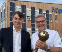 zwei Männer mit Pokal vor Holzgebäude mit PV-Fassade - Energy Globe für Bauteilaktivierung bei my-PV
