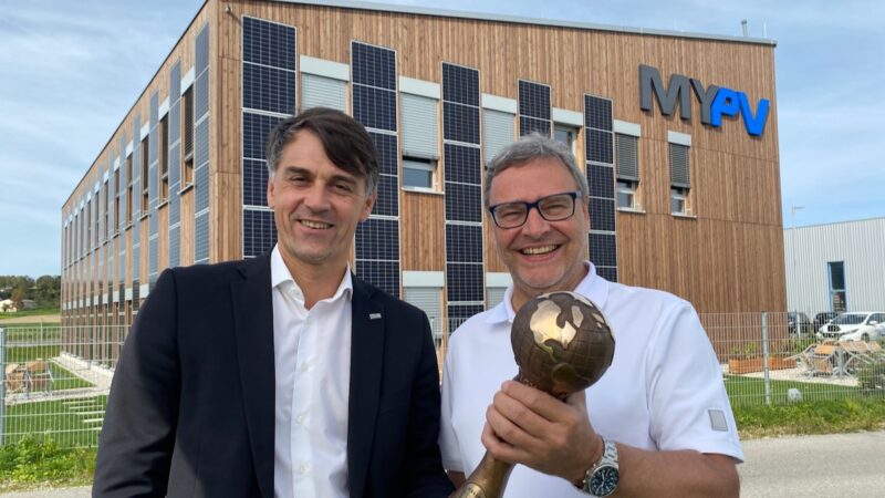 zwei Männer mit Pokal vor Holzgebäude mit PV-Fassade - Energy Globe für Bauteilaktivierung bei my-PV