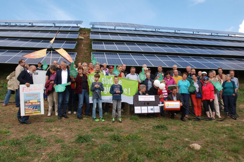 Gruppenfoto einer Bürgerenergiegesellschaft von Modulreihen eines Fotovoltaik-Solarparks