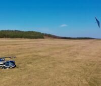 Wiese mit LKW mit Seilwinde und Drachen vor blauem Himmel: der 30-kW-Demonstrator der Flugwindkraftanlagen von EnerKite.