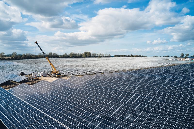 Inmitten einer großen Freiflächen-PV-Anlage arbeitet ein Kran.