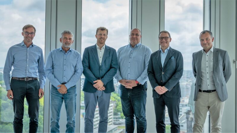 Sechs Männer im leichten Business-Outfit vor einem Fenster