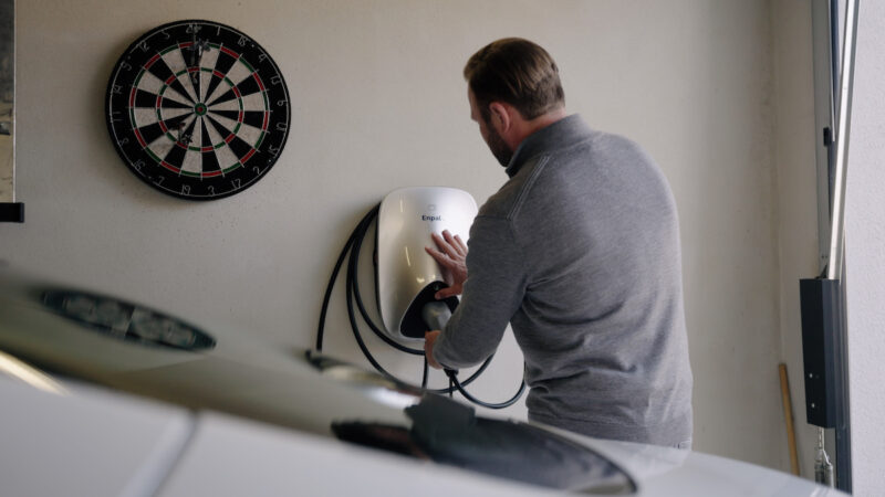 Ein Mann greift nach dem Ladekabel an der Wallbox von Enpal