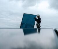 Monteur mit PV-Modul hinter einem PV-Dach.