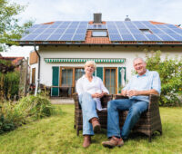 Älteres Paar vor Einfamilienhaus mit Photovoltaik-Anlage