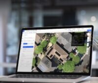 Blick auf einen Laptop-Bildschirm, der ein Luftbild eines Hauses mit Photovoltaik-Anlage zeigt - Planung in der Cloud