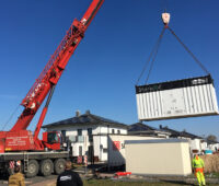 Ein Kran hebt einen Speichercontainer für eine Neubausiedlung.