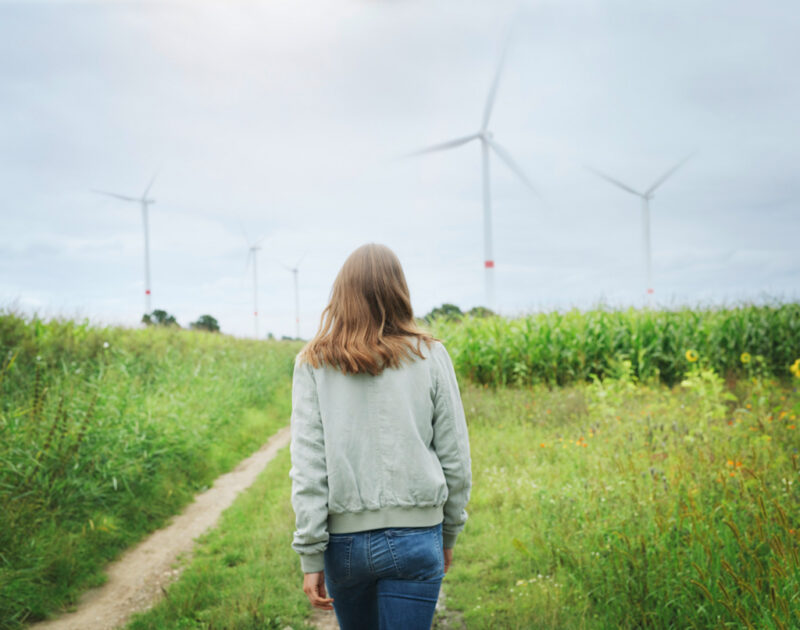 Eine Frau geht auf einem Feldweg auf einen Windpark zu - Symbol für regionalen Ökostrom von E.on