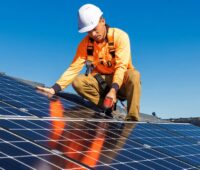 Ein Installateur auf mit Dach schraubt Solarmodule, Eon hat Umfrage zur Photovoltaik durchgeführt.