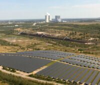 Aufnahme aus Vogelperspektive mit Solarpark im Vordergrund und Braunkohle-Kraftwerk im Hintergrund.