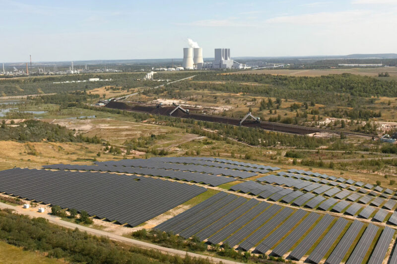 Aufnahme aus Vogelperspektive mit Solarpark im Vordergrund und Braunkohle-Kraftwerk im Hintergrund.