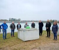 9 Personen vor einem Baggersee mit schwimmender Photovoltaik-Anlage.