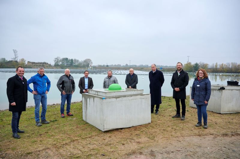 9 Personen vor einem Baggersee mit schwimmender Photovoltaik-Anlage.