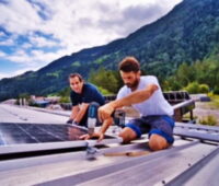 Montage von Solarmodulen auf Metalldächern vor Schweizer Bergpanorama.