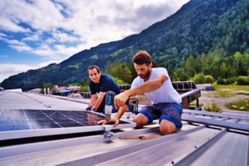 Montage von Solarmodulen auf Metalldächern vor Schweizer Bergpanorama.