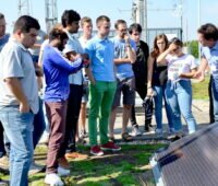 Studenten hören im Freien einem Lehrer zu, der an einem Photovoltaikmodul steht.