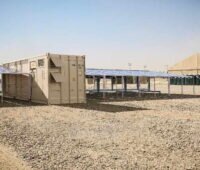 Ein Container eingerahmt von Photovoltaikmodulen in der Wüste.