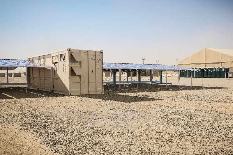 Ein Container eingerahmt von Photovoltaikmodulen in der Wüste.
