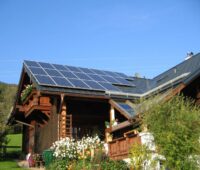 Auf einem Bauernhaus ist eine PV-Anlage installiert. Im Vordergrund sind Blumen gepflanzt.