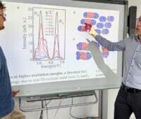 Zwei Männer vor einer Leinwand mit Projektion zu organischer Farbstoff-Solarzelle