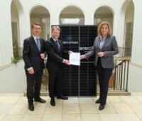 Eine Frau und zwei Herren in einem Ministeriumsgebäude vor Solarmodule und mit Verträgen.