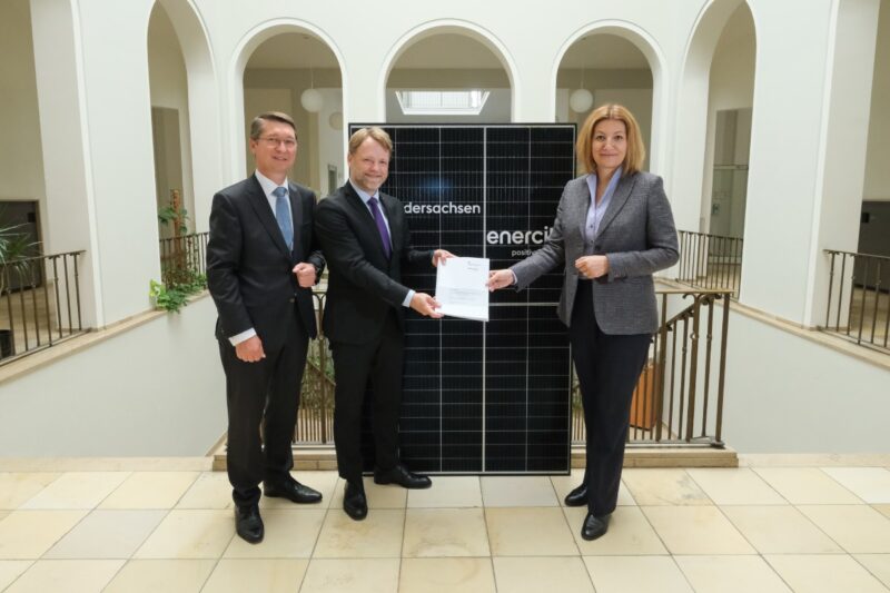 Eine Frau und zwei Herren in einem Ministeriumsgebäude vor Solarmodule und mit Verträgen.