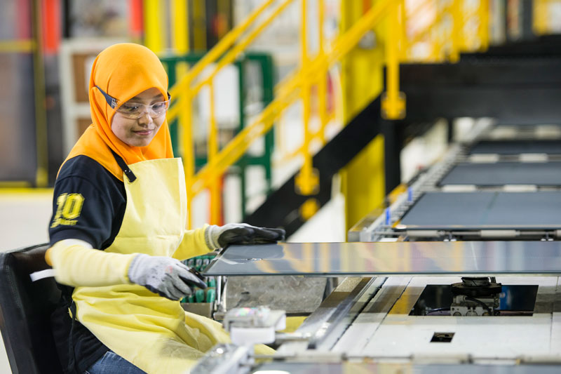 Produktions-Mitarbeiterin mit orangem Kopftuch kontrolliert Photovoltaikmodule in der First-Solar-Fabrik in Malaysia