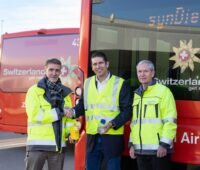 Drei Männer mit gelben Warnwesten vor roten Flughafen-Bussen: Vertrag über Solar-Treibstoff von Synhelion.