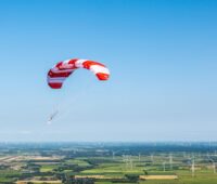 Flugwindenergieanlage über flacher Landschaft mit klassischen Windenergierädern.