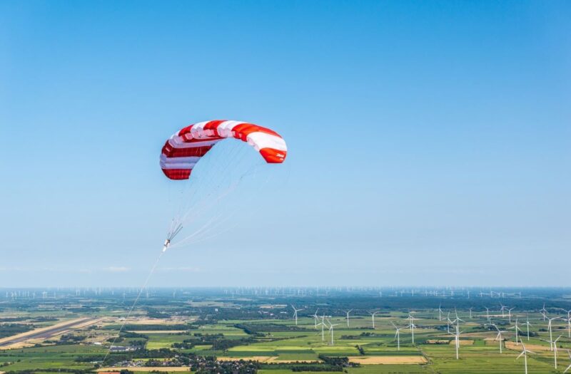Flugwindenergieanlage über flacher Landschaft mit klassischen Windenergierädern.