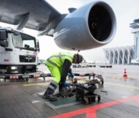 Ein Arbeiter hantiert mit einem tankstutzen unter der Turbine eines Flugzeugs.