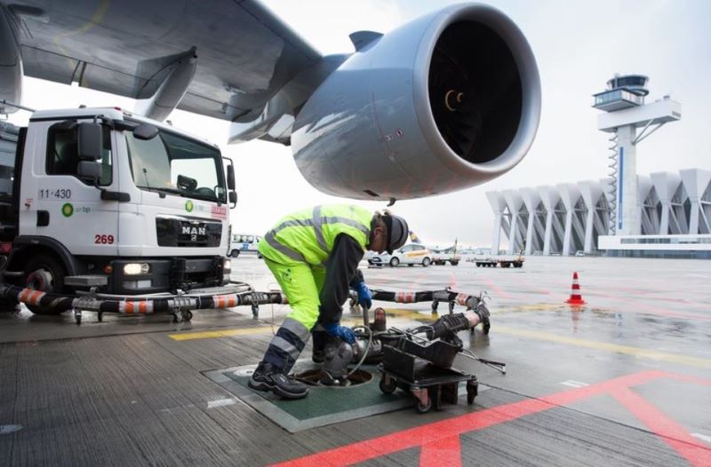 Ein Arbeiter hantiert mit einem tankstutzen unter der Turbine eines Flugzeugs.