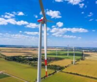 Windkraftanlagen stehen in der Landschaft vor blauem Himmel mit weißen Wölkchen.