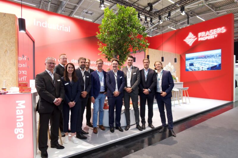 10 Personen in Business-Outfit auf einer Bühne in einer Halle mit Präsentation und dem Schriftzug Frasers.