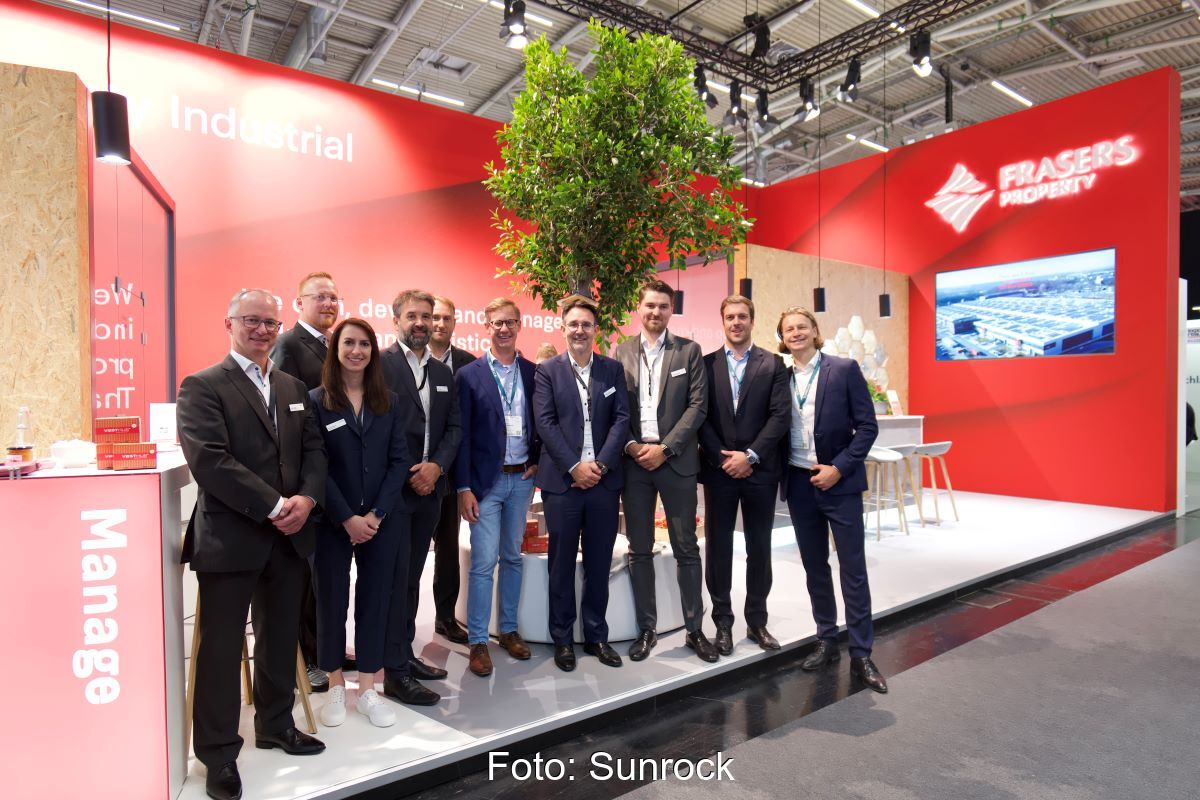 10 Personen in Business-Outfit auf einer Bühne in einer Halle mit Präsentation und dem Schriftzug Frasers.