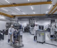 Blick in einem Raum des Fraunhofer ISE mit einigen kleinen Maschinen und Menschen, die sie bedienen. Hier finden praxisnahe Studien für die PV-Produktion statt.