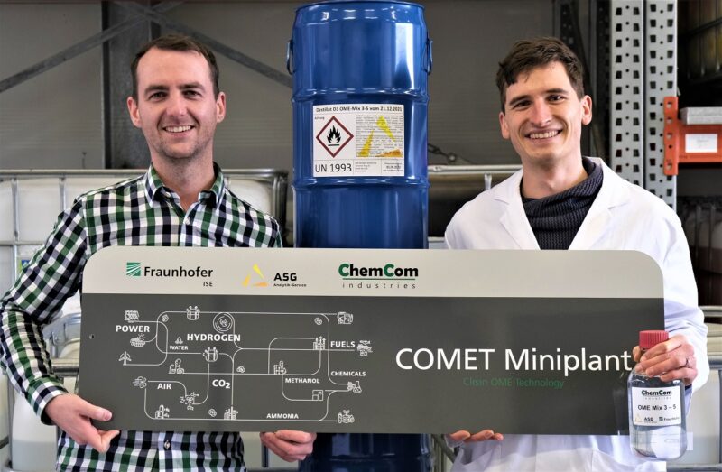 Zu sehen sind zwei Forscher, die ein Schema zeigen, wie Oxymethylenether als Dieselersatz hergestellt wird.