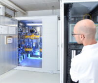Ein Forscher im weißen Kittel blickt im Labor in einer Wasserstoff-Pilotanlage