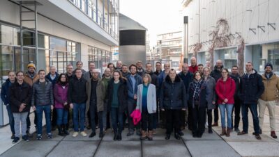 Dutzende Personen beim Gruppenfoto zwischen Institutsgebäuden.