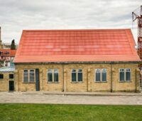 Im Bild eine historische Turnhalle, die mit einer ziegelroten Photovoltaik-Anlage mit MorphoColor-Beschichtung der Solargläser versehen ist.