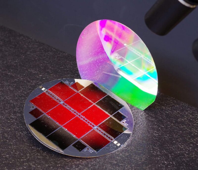 Zu sehen ist die Tandem-Photovoltaik. Die oberste Teilzelle leuchtet rot.. Die nanostrukturierte Rückseite schimmert in Regenbogenfarben.