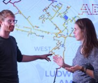 Im Bild Dr. Matthias Eimer und Johanna Heidrich vor einer Karte eines Fernwärmenetzes, die Simulationssoftware soll Fernwärme effizienter machen.