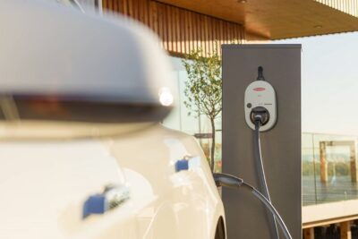 Blick auf die Fronius Ladestation Watt Pilot. Im Vordergund ein weißes Elektroauto