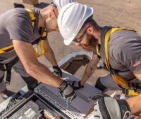 Zwei Monteure mit Schutzhelmen arbeiten im Freien an einem Wechselrichter