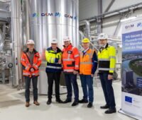 Die fünf Verantwortlichen stehen vor einem Stahltank in der Flusswärmepumpen-Anlage Mannheim.